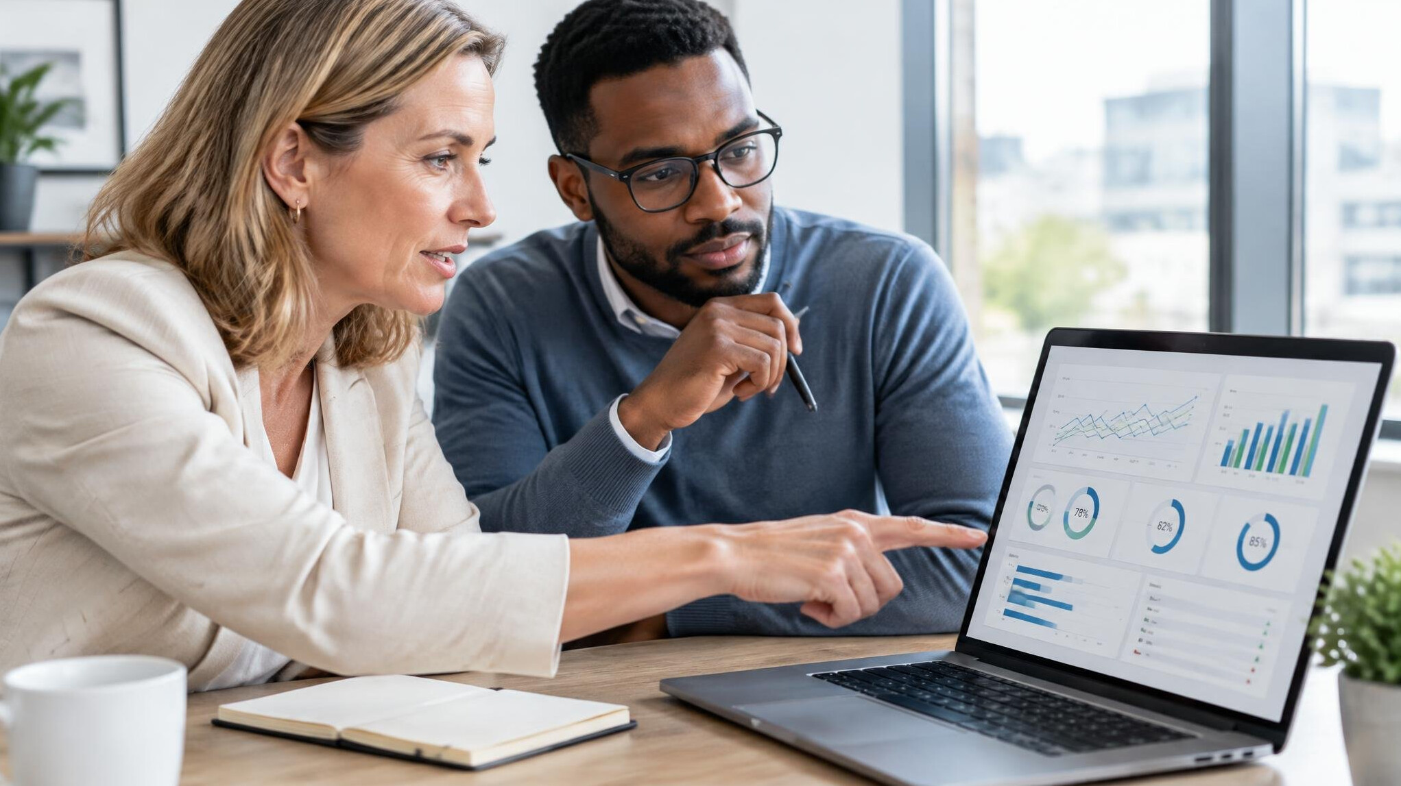 Two colleagues analyzing management performance data on a laptop in an office